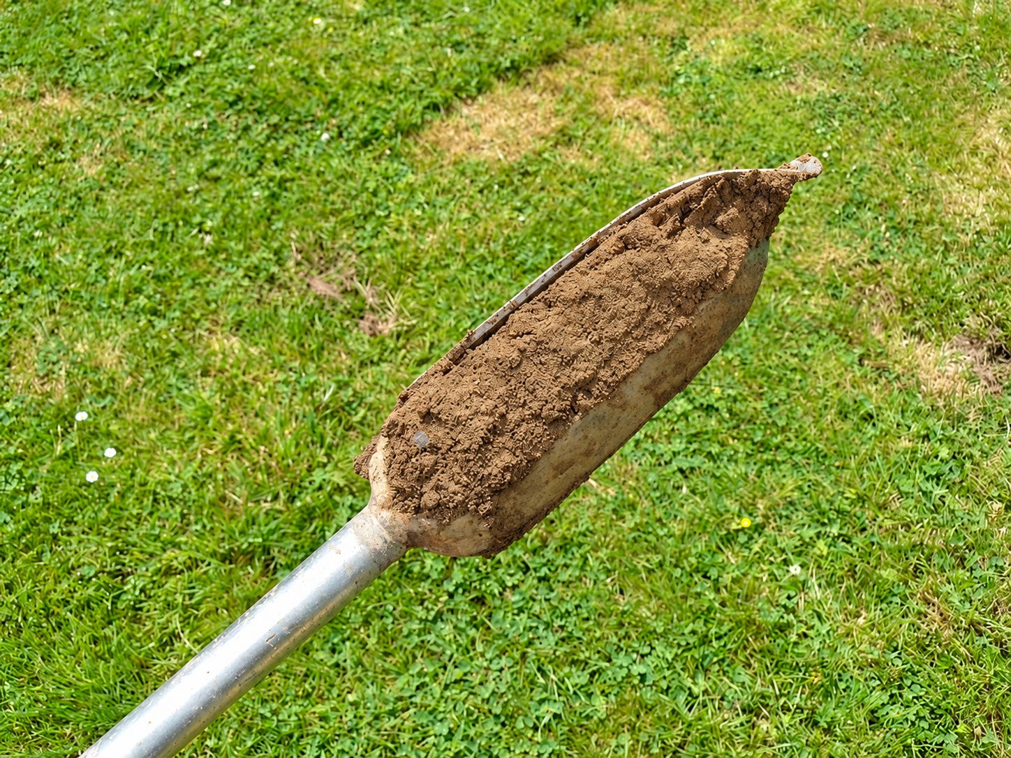 Une tarière métallique remplie de terre brune au-dessus d’une pelouse verte