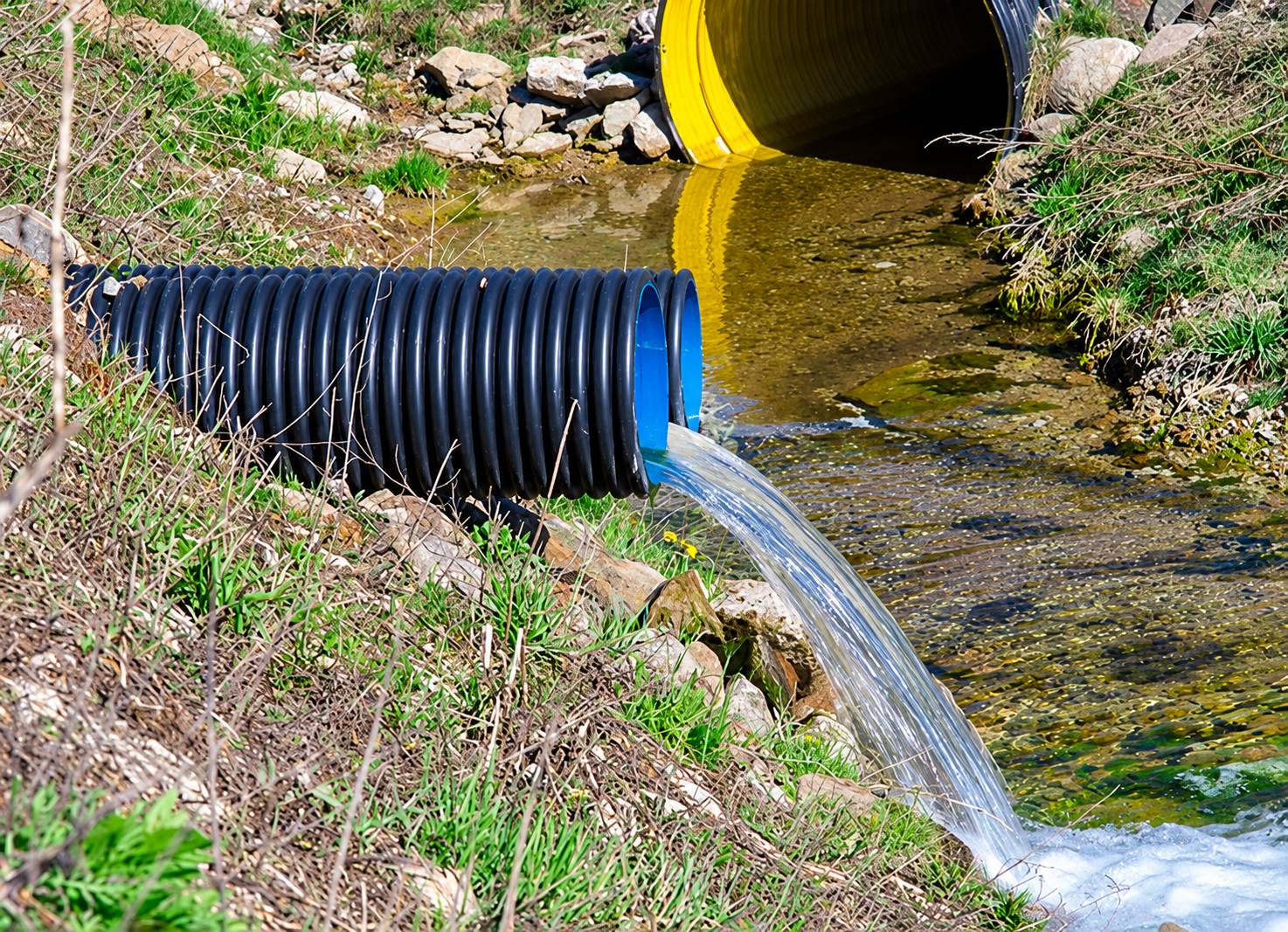 Un tuyau de drainage noir annelé rejette un jet d’eau dans un fossé